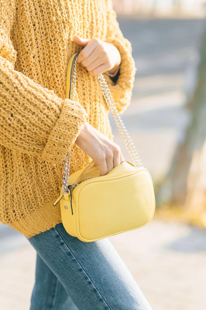 A stylish yellow bag paired with a knitted sweater and denim jeans outdoors.